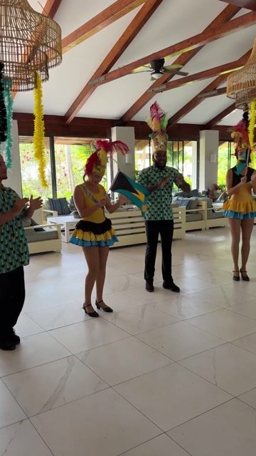 People in colorful traditional African attire dancing together in a bright, modern indoor venue with exposed wooden beams and decorative woven light fixtures.