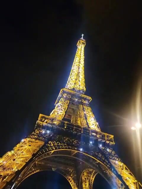 The illuminated Eiffel Tower at night shot from below, highlighting its golden lights and iron lattice structure against a dark sky.