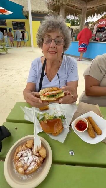 A woman enjoying a viral chicken mozzarella marinara sandwich at an outdoor beach venue with colorful architecture.